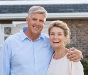 Portrait of a happy senior couple smiling in front of their house. Older couple embracing and looking at camera. Happy old retired couple hugging.
